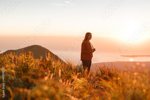 Carefree happy woman in sweater enjoying nature on grass meadow on top of mountain with sunrise. Beauty girl outdoor with sunbeams. Freedom concept © Yevhenii