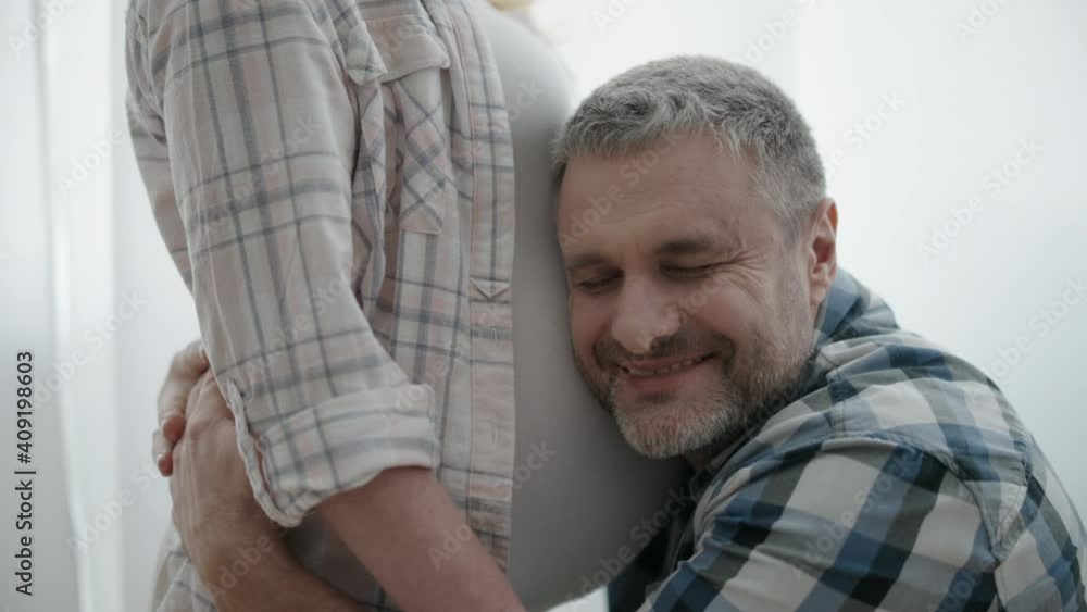 Excited man hugging pregnant wife, kissing belly, prenatal bonding with baby Excited man hugging pregnant wife, kissing belly, prenatal bonding with baby