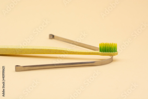 metal scraper or tongue cleaning brush and a toothbrush on beige background. Hygiene of the oral cavity