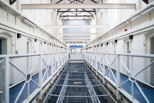 Looking into prison cell block victorian British English jail house with bed in room lock up high security room derelict old new category A B C in custody with bars door open confined escaping