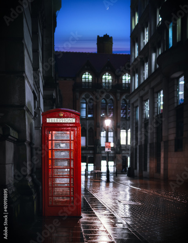 Deserted street at night with traditional royal red British telephone phone box lit up light reflecting on water after rain clear night sky moon eerie view city centre England UK © Matthew