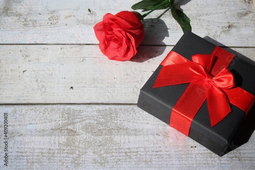 Romantic, love and Valentine's day concept. Gift box with red ribbon and red rose on wooden table