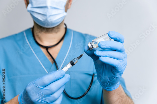 Doctor with blue surgical gloves dials a coronavirus vaccine into a syringe to vaccinate against a worldwide epidemic coronavirus covid-19. Healthcare And Medical concept