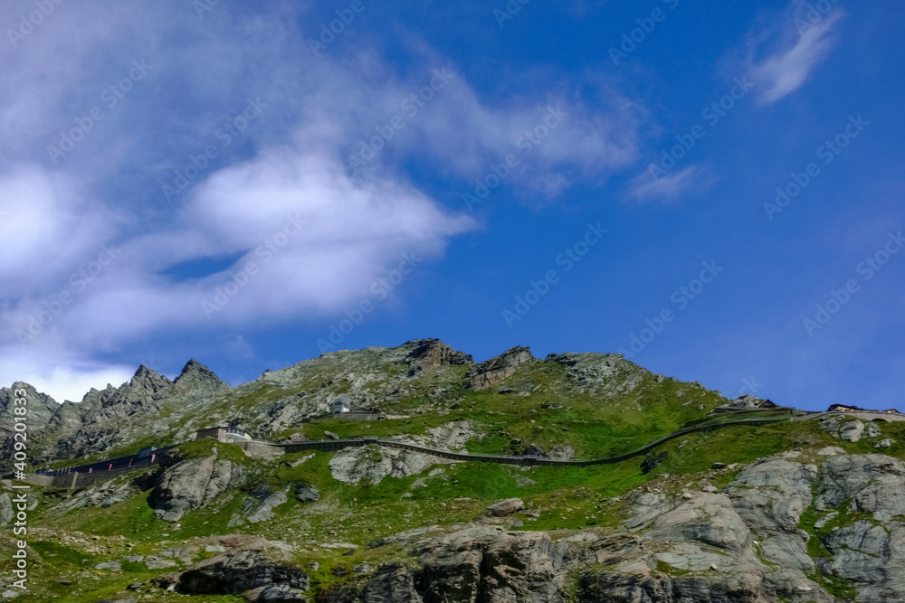 curvy road with a house on a rocky mountain with blue sky and clouds