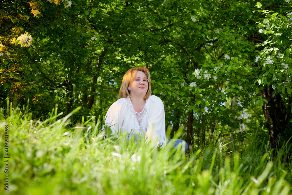 Outdoor portrait of a beautiful blonde middle-aged woman near blossom apple trees with white flowers. Outdoor portrait of a beautiful blonde middle-aged woman near blossom apple trees with white flowers.