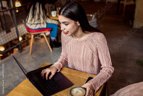 Portrait of young woman using laptop in coffee shop.