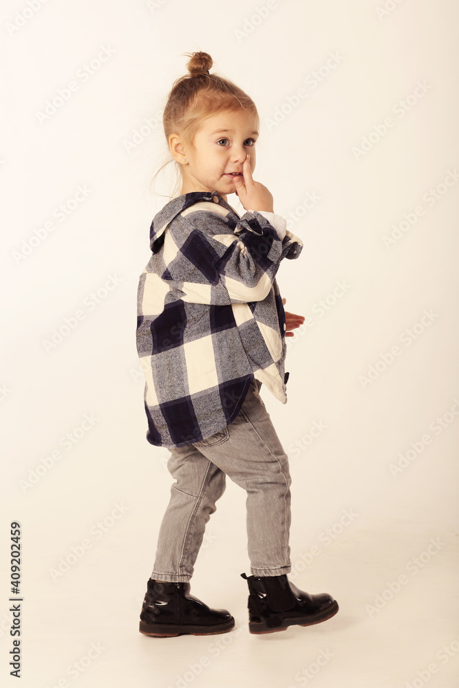 cute little blond baby girl in black boots, jeans, checkered shirt with copy space cute little blond baby girl in black boots, jeans, checkered shirt with copy space