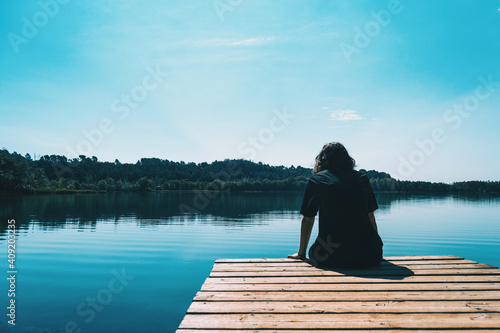 girl sitting on the edge of Banyoles lake with the landscape reflected in the water