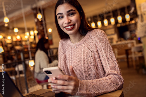 Portrait of young woman using smartphone in coffee shop.