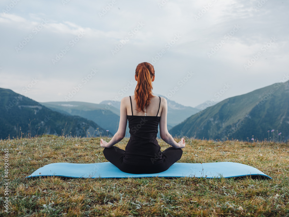 Woman sits on fitness mats and meditates yoga asana outdoors in the mountains