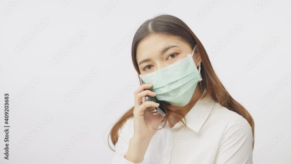 Young woman has her surgical mask on while using her phone, film in slow motion against white background Young woman has her surgical mask on while using her phone, film in slow motion against white background