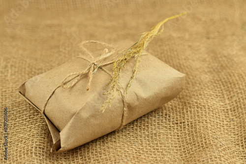 Simple eco friendly gift box package wrap with brown paper. Burlap background. Delivery of ecological products, eco-friendly packaging, craft. Green present concept, copy space.