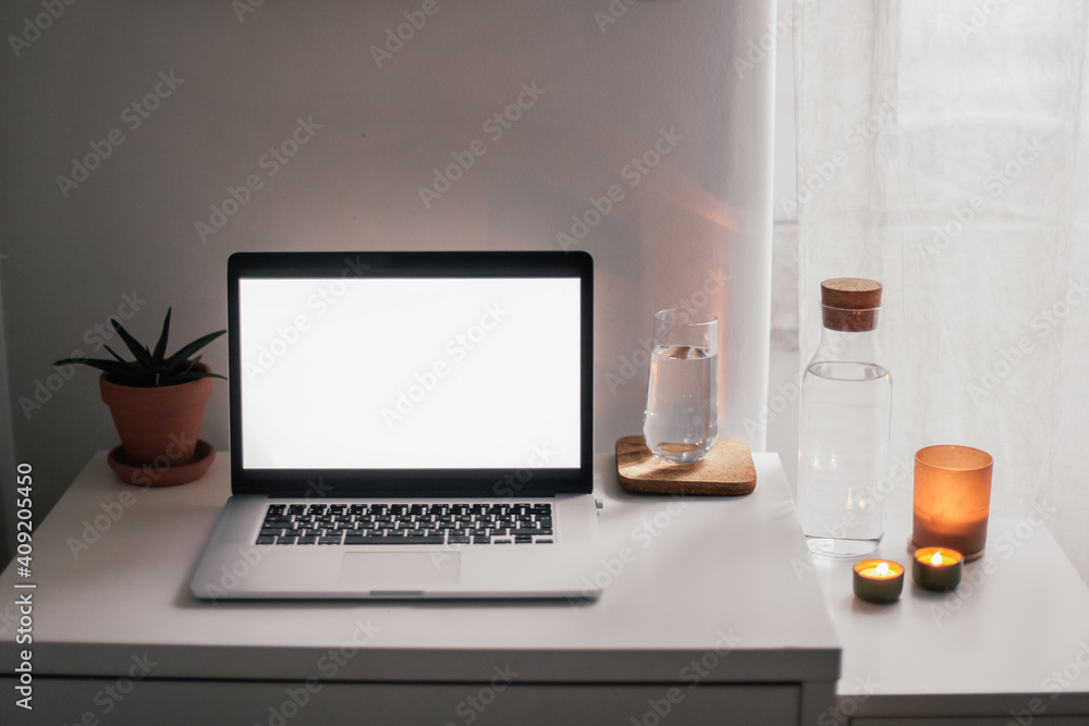 A laptop with white screen on a white table. An aloe plant, a glass of water, candles on the background A laptop with white screen on a white table. An aloe plant, a glass of water, candles on the background