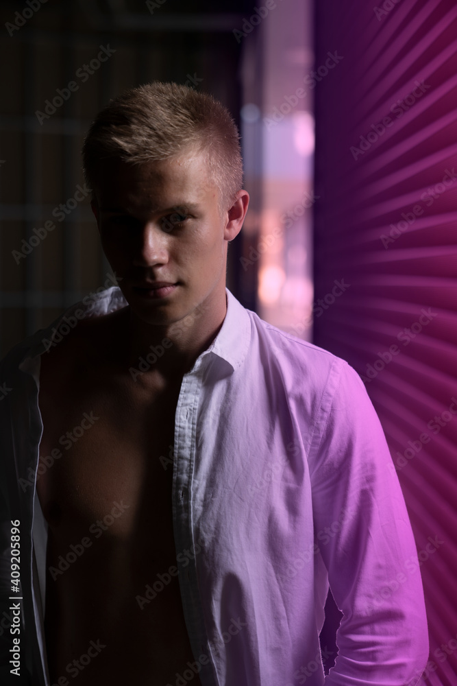 a young handsome guy stands in a poorly lit place near a shop window that gives off a lilac glow a young handsome guy stands in a poorly lit place near a shop window that gives off a lilac glow