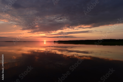 Sky in the brightly lit twilight of a sunset over picturesque lake water with reflection clouds and sunbeam on the horizon over the water surface