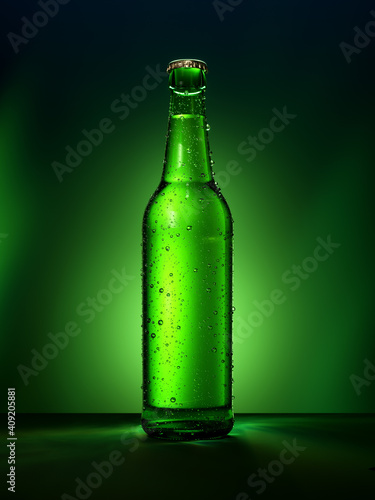 Single green beer bottle with water drops against green illuminated background.