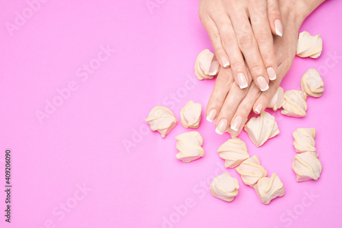 Beautiful Female Hands with French manicure and marshmallows over colorful pink paper background