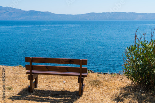 Empty wooden bench, on edge of grassy cliff, facing the ocean. Travel magazine cover concept
