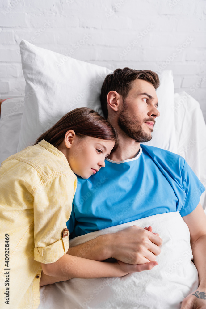 girl leaning on father lying on hospital bed and holding his hand girl leaning on father lying on hospital bed and holding his hand