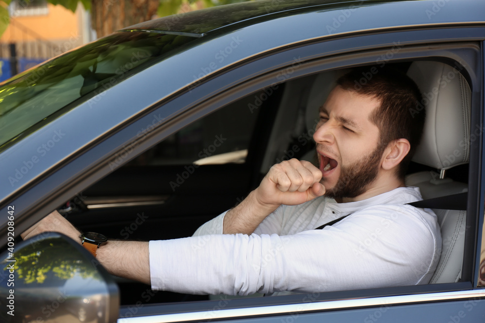 Tired man yawning in his modern car