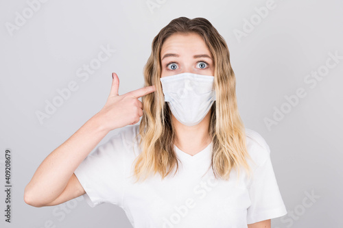 Young attractive woman points her finger at a medical protective mask on her face. Prevention of coronavirus infection and colds.