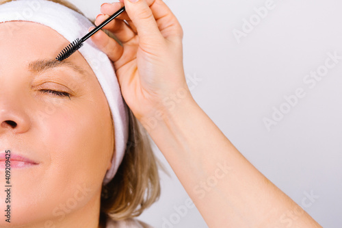 Enlarged photo where the hand of the master makes the lamination of the eyebrows of a woman with a bandage on her head. Fashion trends on a white background.