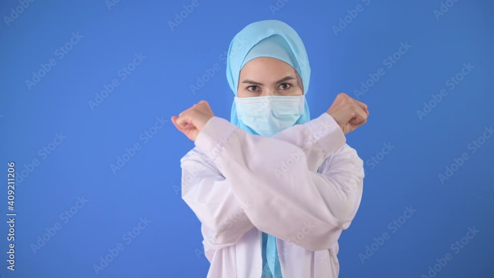 Female muslim doctor with hijab wearing a surgical mask over blue background studio. Female muslim doctor with hijab wearing a surgical mask over blue background studio.