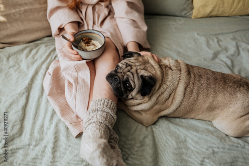 A girl has breakfast in bed with a pug