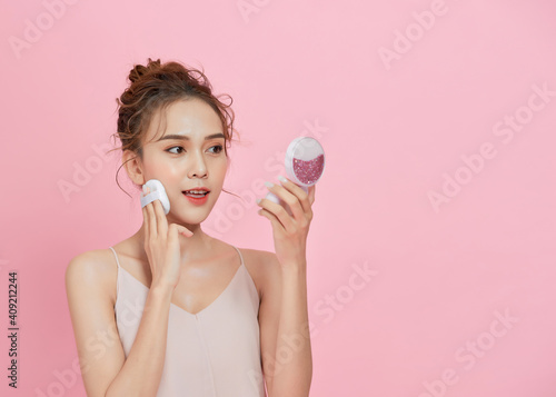 Фотография Young attractive Asian lady applying blusher on her face with powder puff over pink background