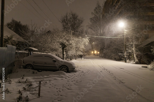 under the light of the streetlights, cars in the parking lot were covered with snow, problems for car owners due to a heavy snowstorm, winter snowdrifts in the city
