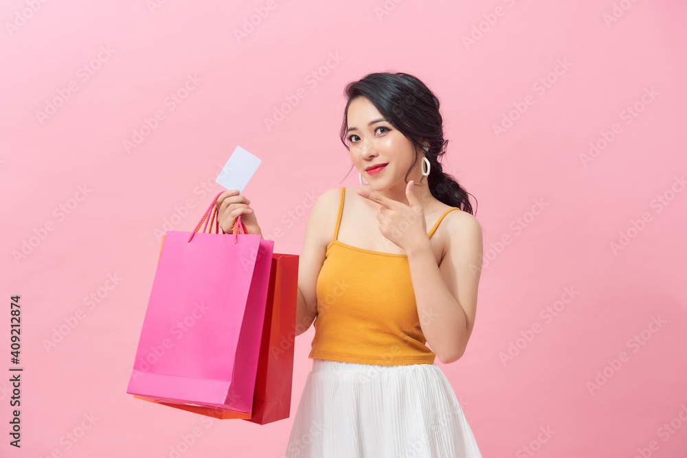 Portrait of a beautiful girl wearing dress and holding colorful shopping bags and showing credit card isolated over pink background
