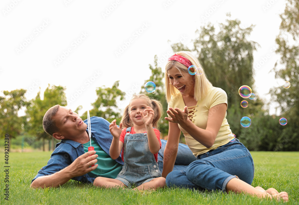 © New Africa - Happy family blowing soap bubbles in park on green grass