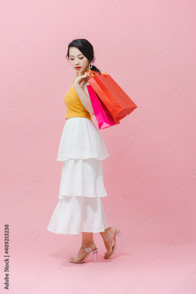 Style asian woman holding shopping bags on pink background.