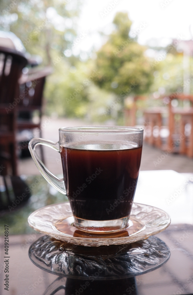 A glass of black coffee on a glass table with a blurred background A glass of black coffee on a glass table with a blurred background