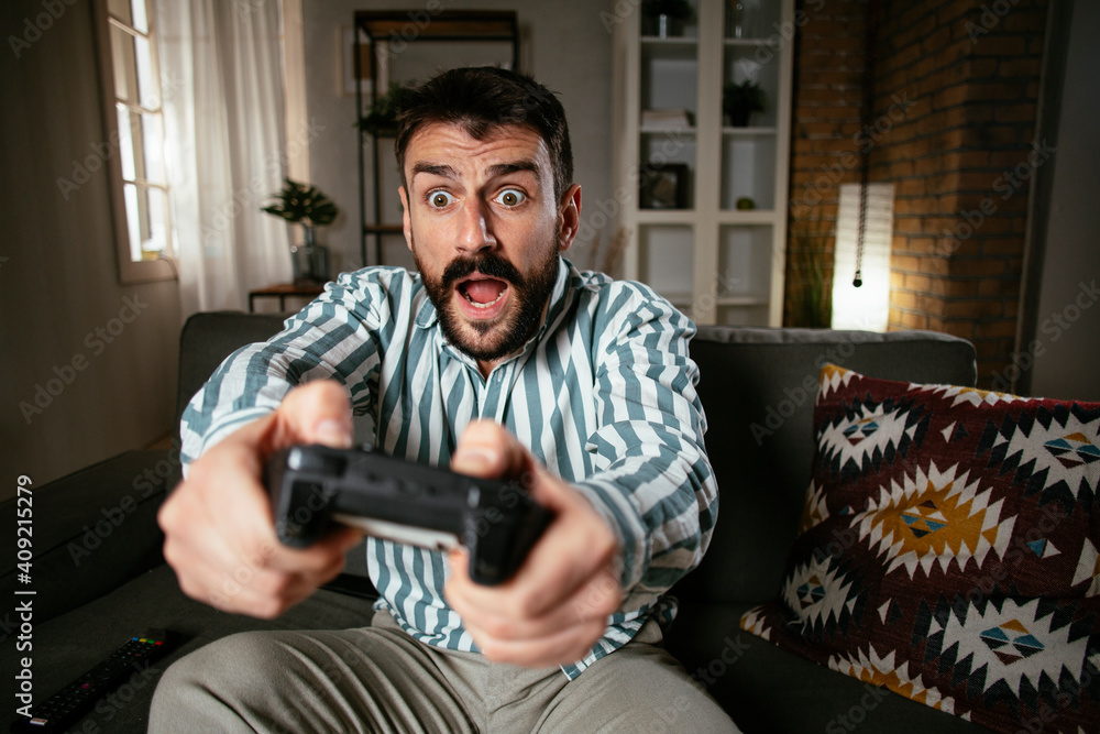 Young attractive man playing video games in the living room. Handsome man having fun at home. Young attractive man playing video games in the living room. Handsome man having fun at home.