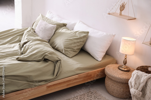 Comfortable bed with olive green linen in modern room interior