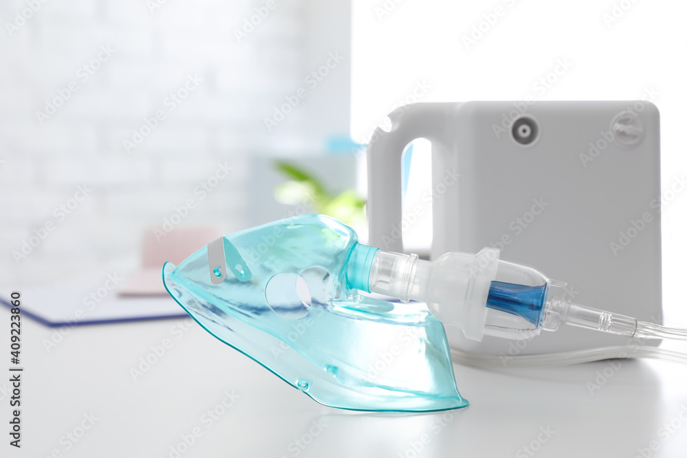 Modern nebulizer with face mask on white table indoors. Equipment for inhalation Modern nebulizer with face mask on white table indoors. Equipment for inhalation