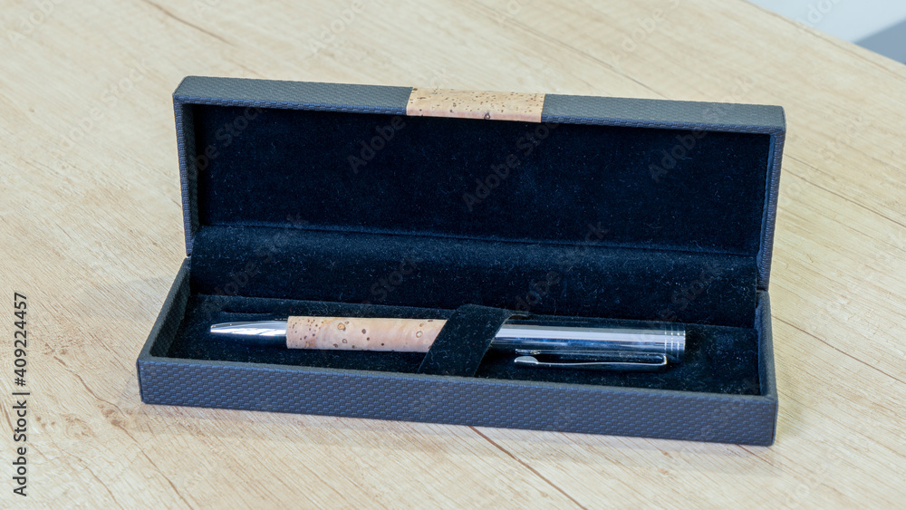 Closeup metal silver pen with a cork element in a gift box. On wooden desk background. Closeup metal silver pen with a cork element in a gift box. On wooden desk background.