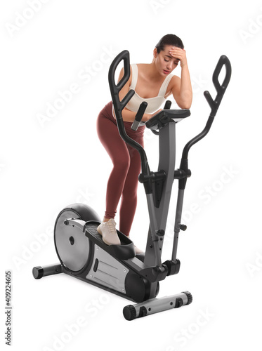 Tired woman after training on modern elliptical machine against white background