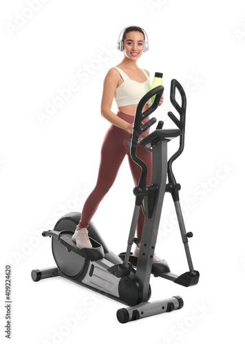 Woman with bottle using modern elliptical machine on white background