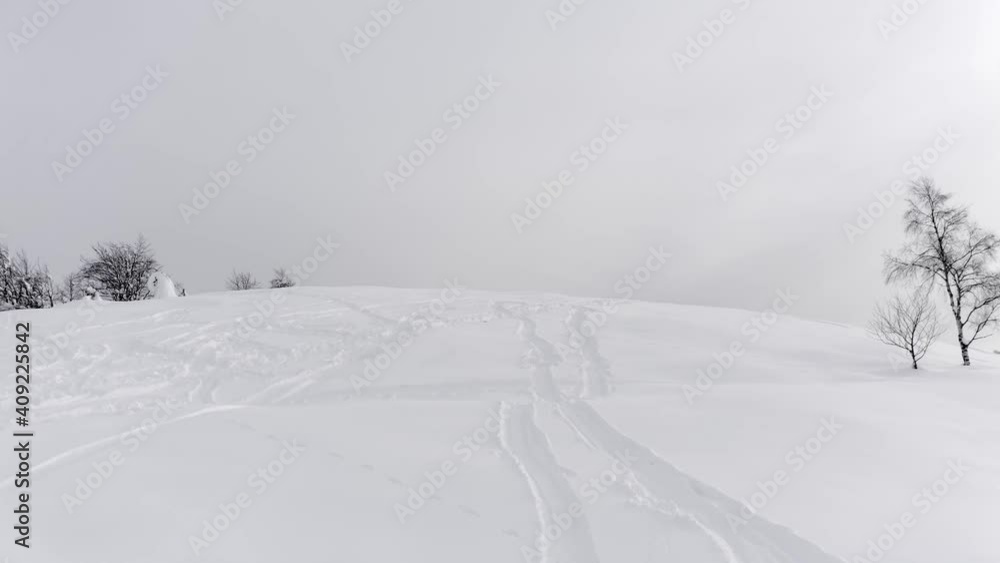 Aerial view of snowy mountain peak with ski tracks on snow in a winter and foggy journey. Some trees on side Aerial view of snowy mountain peak with ski tracks on snow in a winter and foggy journey. Some trees on side