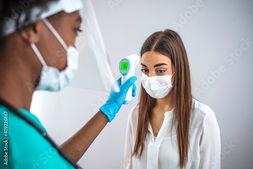 Shot of a young woman getting her temperature taken with an infrared thermometer by a healthcare worker during an outbreak. Woman goes through a temperature checks before going to work