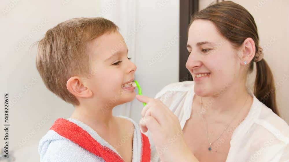 Portrait of little smiling boy brushing and cleaning teeth with his smiling mother in bathroom. Concept of child hygiene and healthcare at home. Caring parents and kids at home. Portrait of little smiling boy brushing and cleaning teeth with his smiling mother in bathroom. Concept of child hygiene and healthcare at home. Caring parents and kids at home.