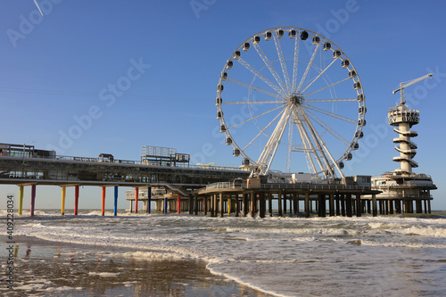 Ferris wheel on De Pier in The Hague Scheveningen on a windy winter day with blue sky and people at the beach, the Netherlands, Europe © tselykh