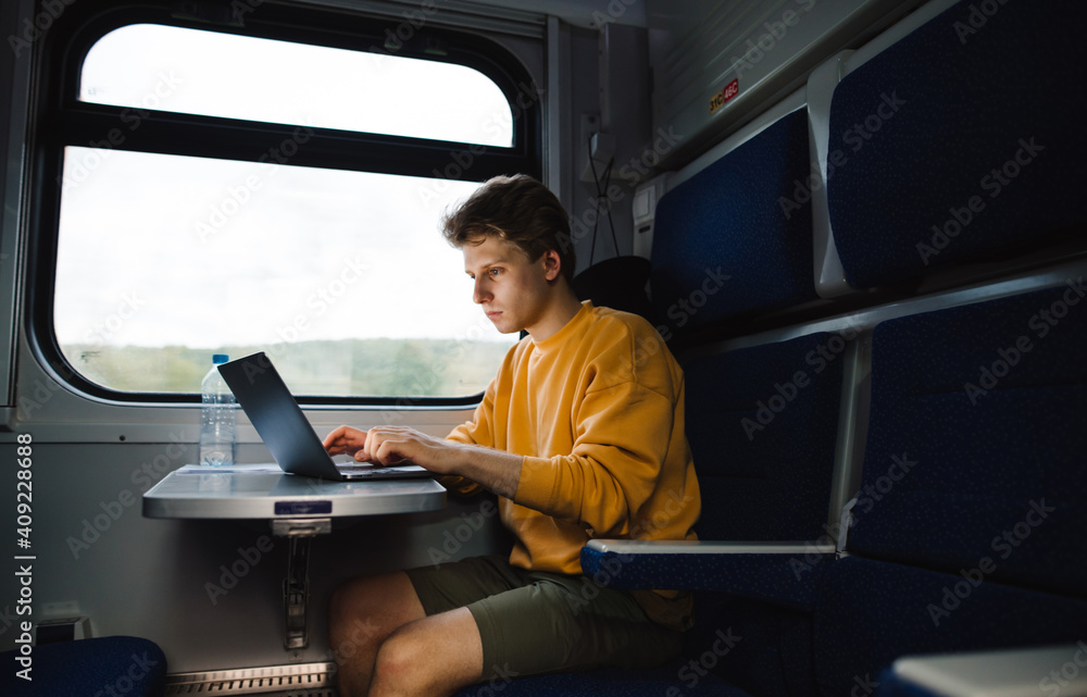 Concentrated male freelancer working online in a train at the table. The guy uses a laptop on the train while traveling. Concentrated male freelancer working online in a train at the table. The guy uses a laptop on the train while traveling.