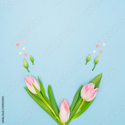 Fototapeta Naklejka Na Ścianę i Meble -  Creative spring composition with green leaves, pink hearts, rosebuds and pastel tulips on blue background. Minimal concept with copy space.