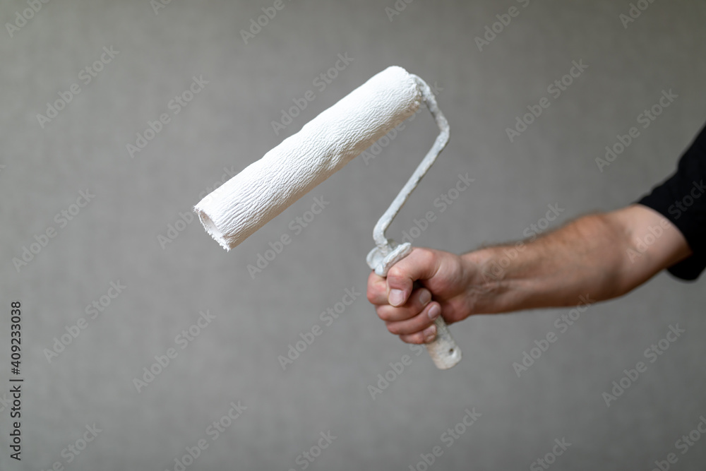 Naklejka premium handyman holds with a roller for painting walls or other surfaces. Roller in white paint. Construction or repair concept.