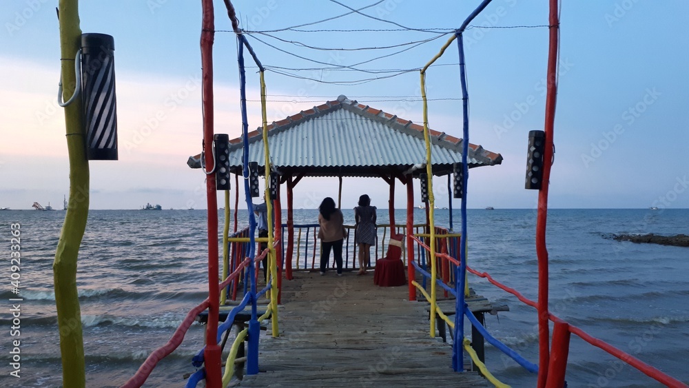 Fototapeta premium two girls standing on the colorful dock by the sea enjoying the sunset