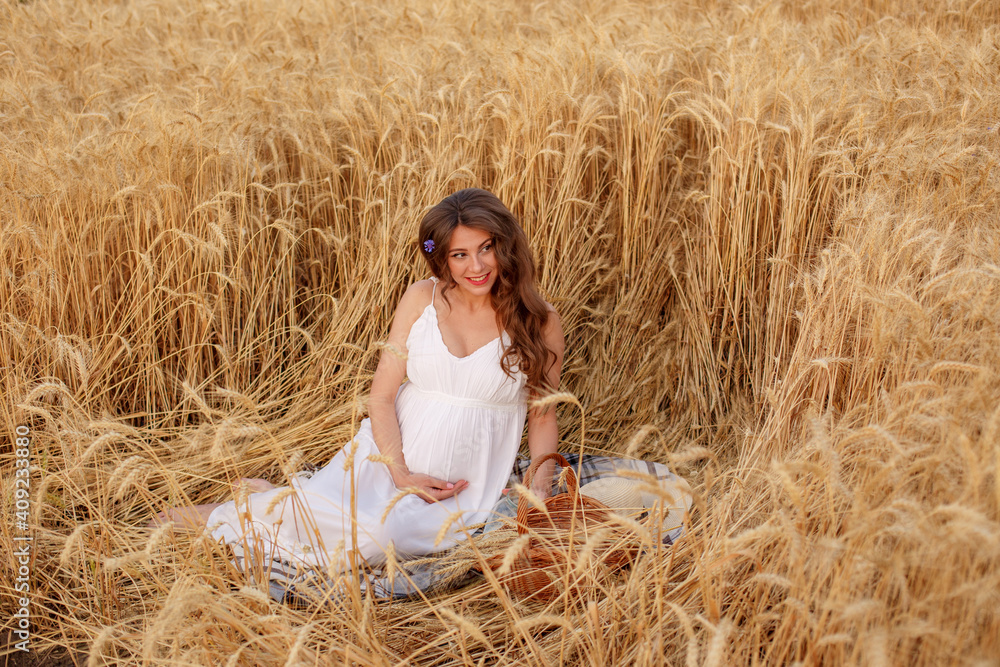 pregnant woman sitting in a field of wheat a picnic