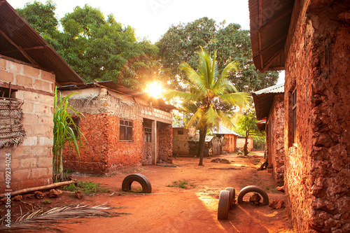 Scenic sunset over african village with palm. Street full of light, vibrant red soil and red color of buildings. Huts along the street. Traditional architecture, Tanzania countryside.